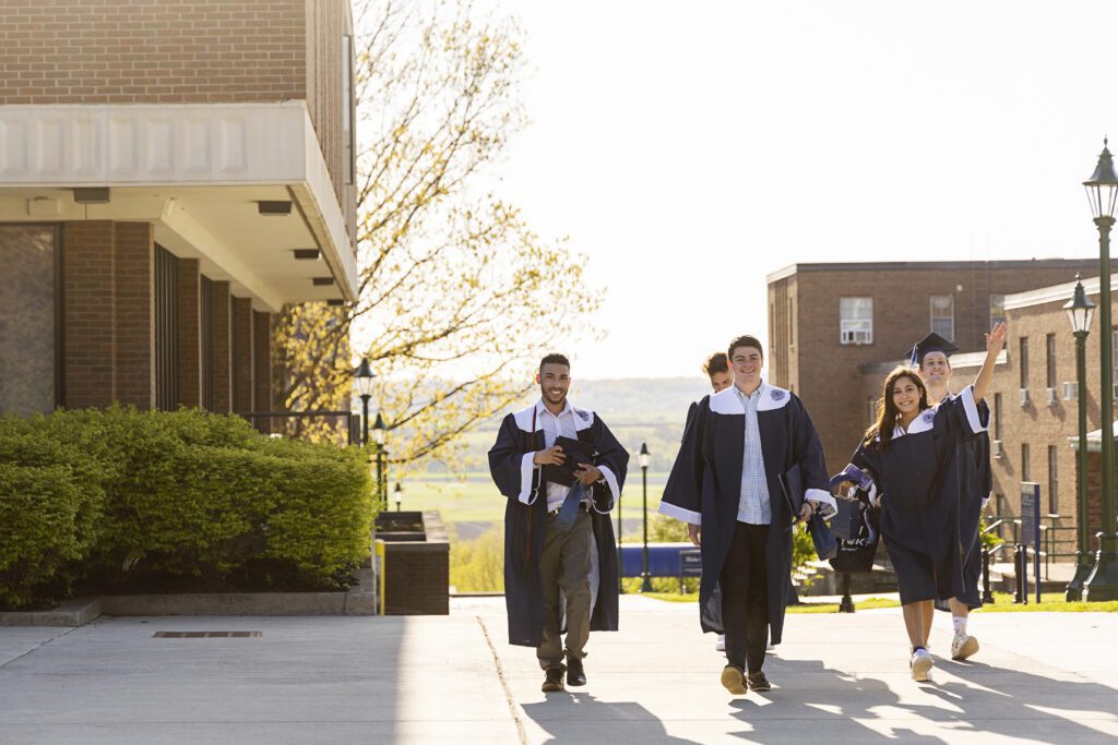 Class of 2021 graduates walk in their cap and gowns by the College Green.