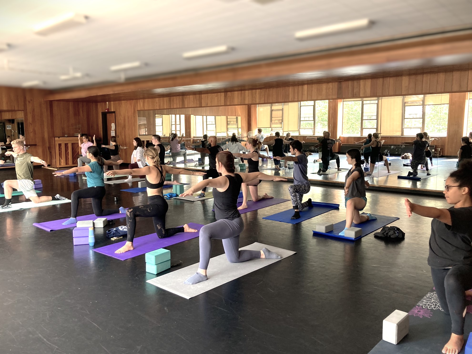 2022, Yoga Class, Schrader Dance Studio, Enhanced Approximately 12 students doing a yoga pose in a kneeling position on yoga mats in the Schrader Dance Studio, where this are mirrors in the background
