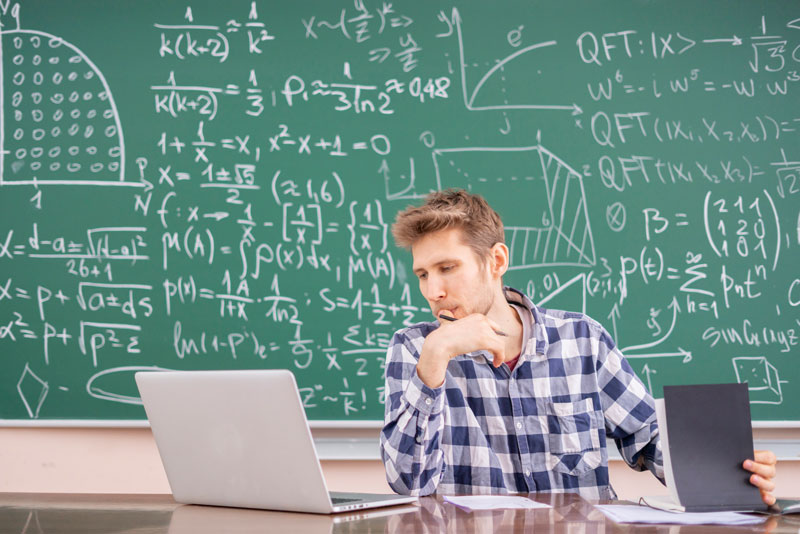 board covered with equations and man sitting with laptop