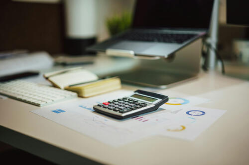 Caluculator on desktop with laptop, keyboard, and charts