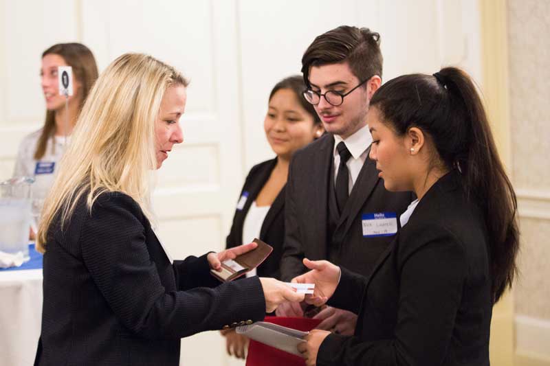 two students exchange business cards with a professional woman at a networking event