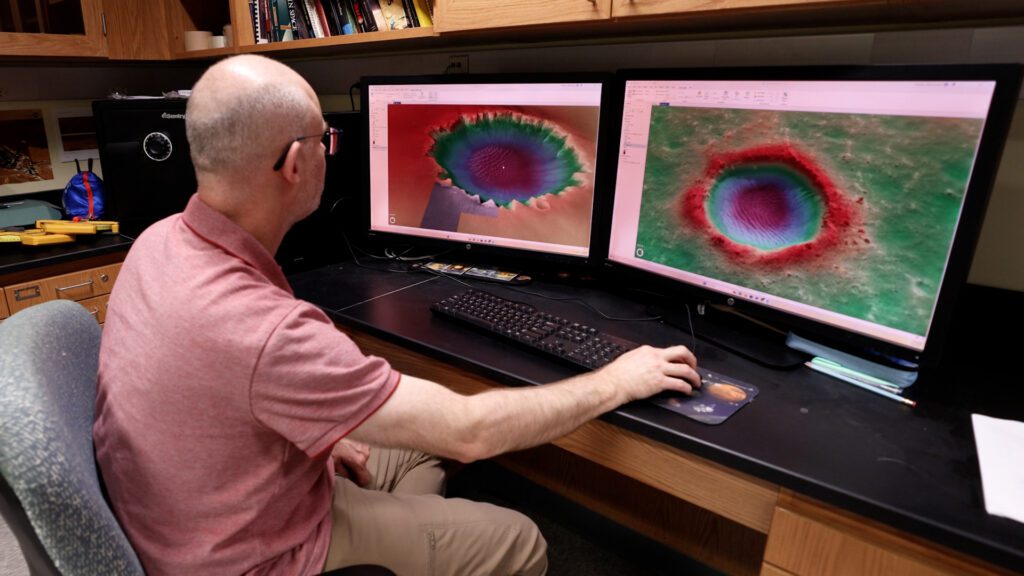 Professor looking at 3D photos of craters on Mars on two computer monitors.